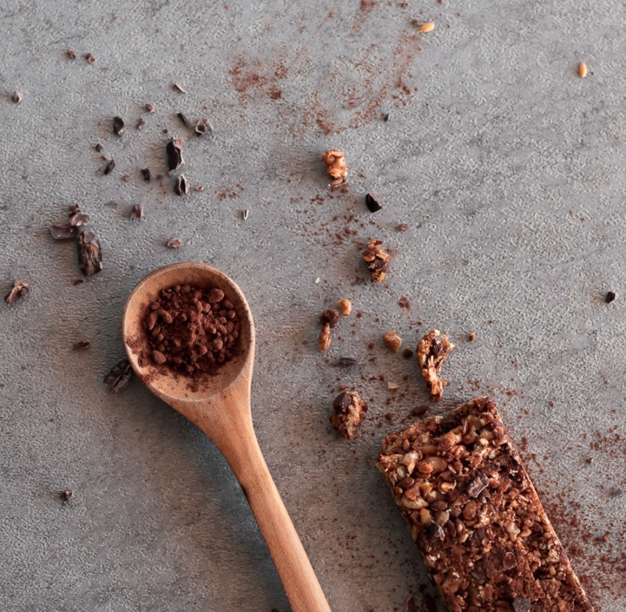 Barre de céréale bio au chocolat noir à côté d'une cuillère de cacao