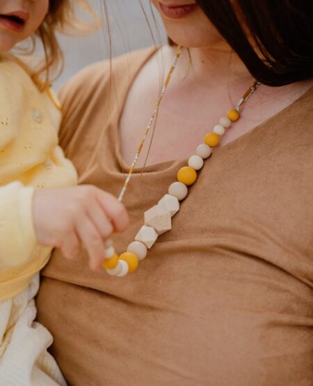 Maman qui porte le collier d'allaitement et de portage capucine jaune et blanc tenue par son bébé