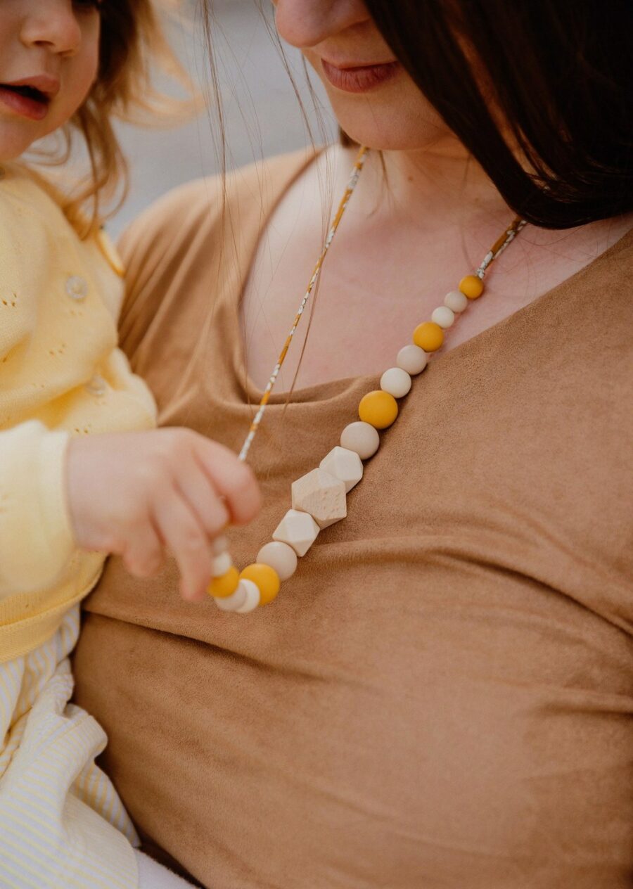 Maman qui porte le collier d'allaitement et de portage capucine jaune et blanc tenue par son bébé