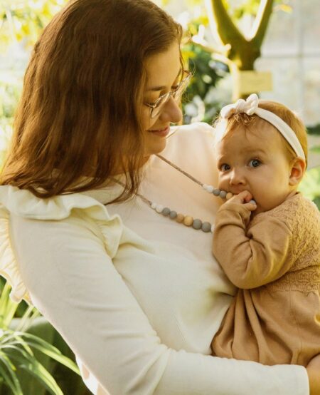 Collier d'allaitement scandi avec des perles blanches, grise en silicone et bois porté par une maman avec bébé qui le machouille
