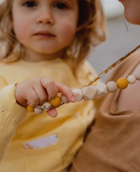 Petite fille porté par sa maman qui tiens le collier d'allaitement et de portage capucine