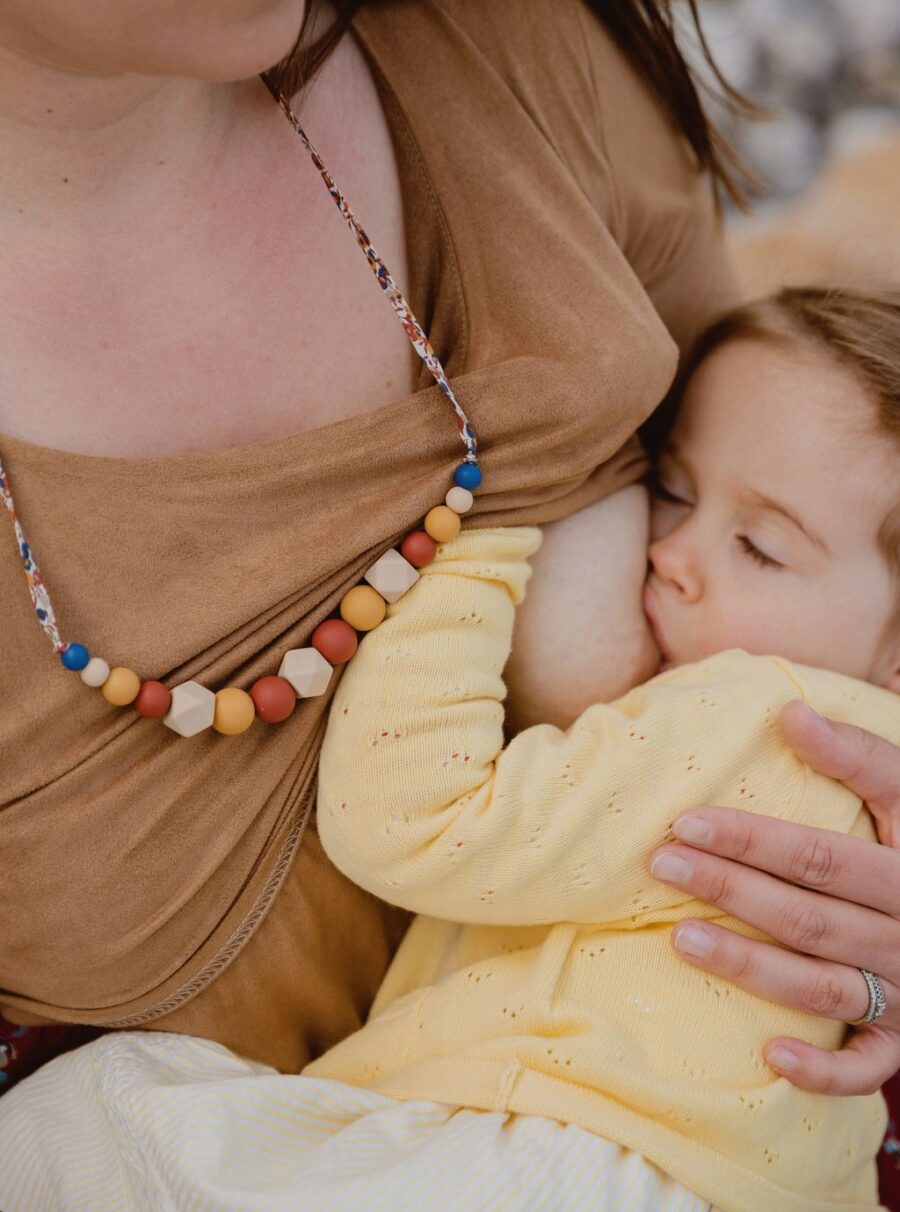 Bébé qui tête le sein de sa mère avec un collier d'allaitement noisette