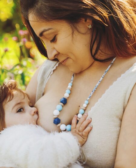 Maman qui allaite son bébé avec un collier d'allaitement et de portage lilas : les perles sont bleus, blanches et beige en silicone