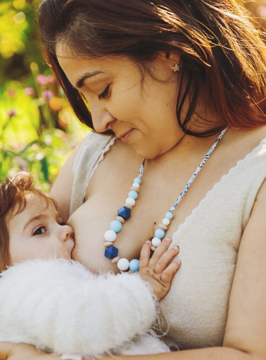 Maman qui allaite son bébé avec un collier d'allaitement et de portage lilas : les perles sont bleus, blanches et beige en silicone