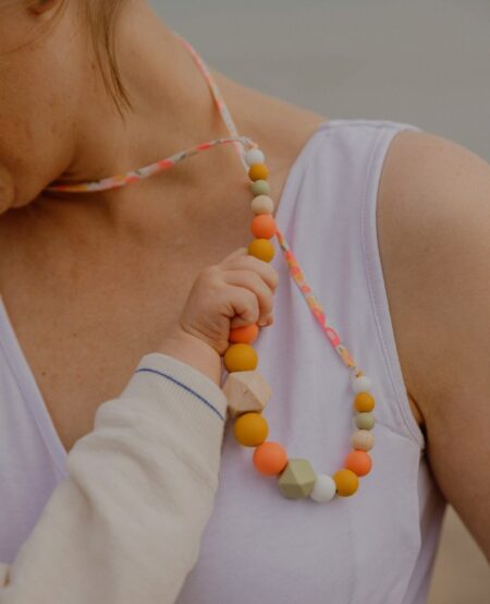 Bébé qui tient le collier d'allaitement sorbet été couleur corail de sa maman