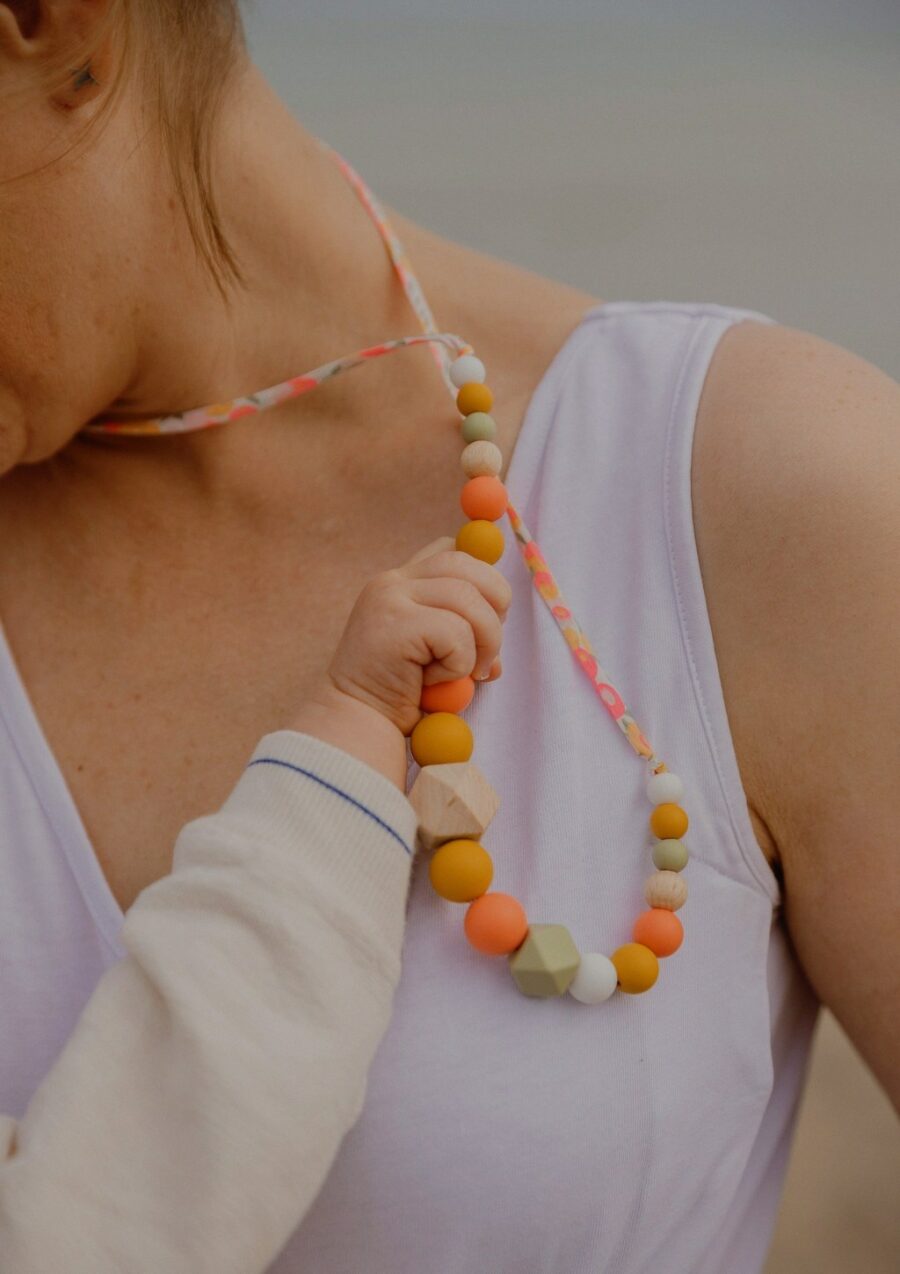 Bébé qui tient le collier d'allaitement sorbet été couleur corail de sa maman