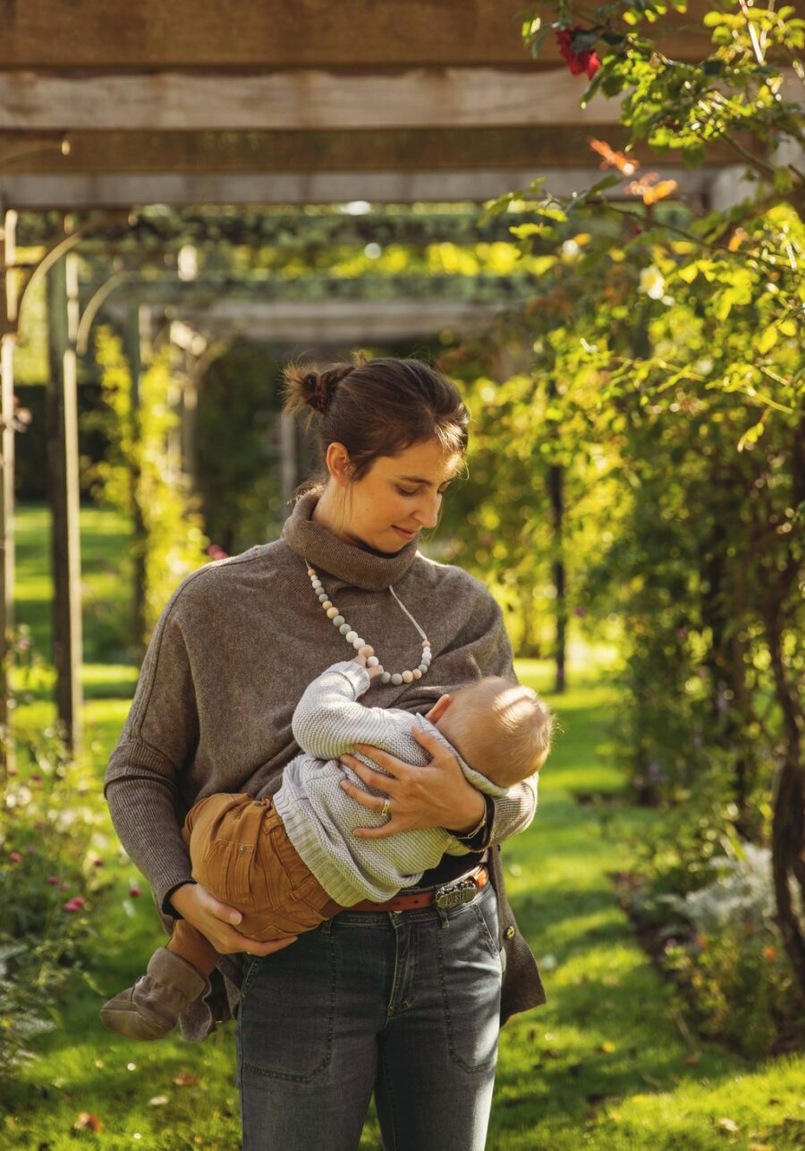 Maman qui porte son bébé qui tient le collier d'allaitement et de portage scandi
