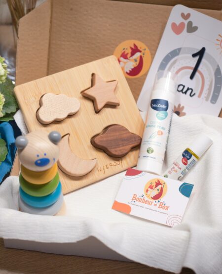 Box bébé avec abonnement qui contient : un puzzle en bois, une carte étape, une crème apaise peau, une tour en anneau, une huile badaboum