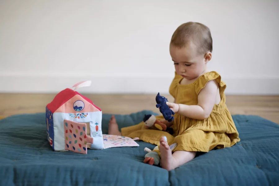 Bébé assis entrain de jouer avec sa maison en tissus et une peluche
