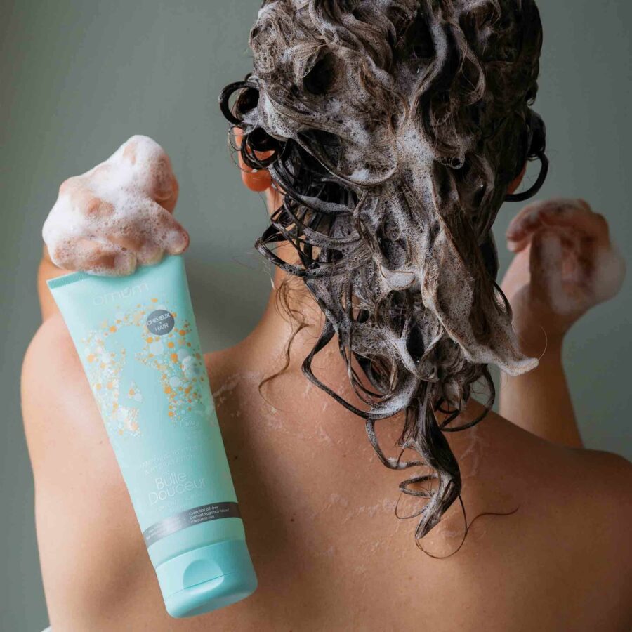Femme qui tient le shampoing bio de Omum dans les mains avec les cheveux savonnés