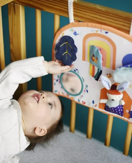 Bébé qui joue avec son tableau d'activité accroché dans son lit
