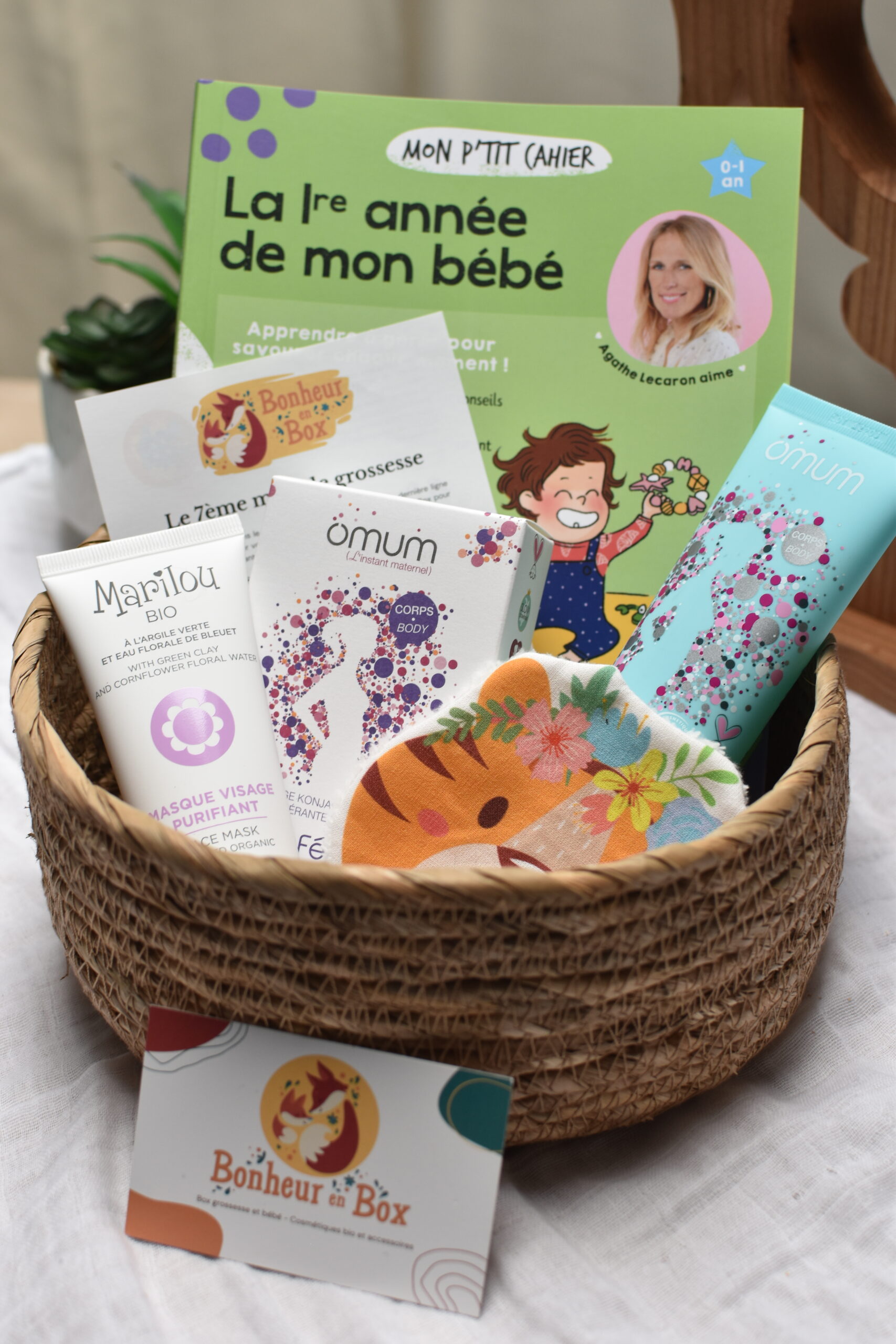 Vue d'ensemble d'une box future maman pour le 7ème mois de grossesse, comprenant un masque visage bio, une éponge konjac, un gel bio pour les jambes lourdes, une lingette lavable faite à la main, et un livre sur la première année de bébé.