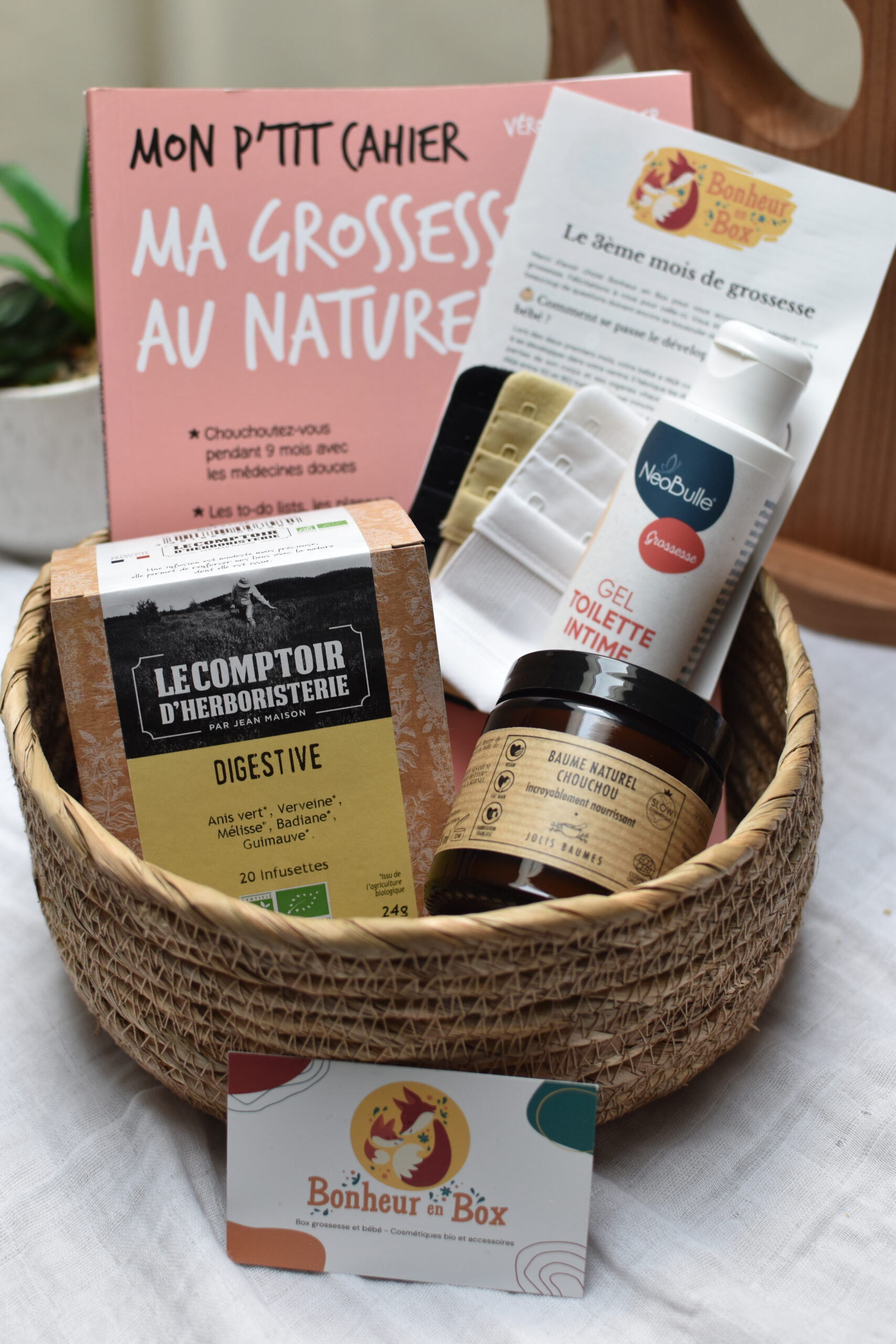 Vue d'ensemble d'une box future maman pour le 3ème mois de grossesse, incluant une tisane bio, un baume bio, un gel de toilette intime bio, des rallonges de soutien-gorge, et un livre Ma grossesse au naturel.